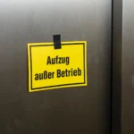 Gelbes Schild mit Aufschrift Aufzug außer Betrieb an geschlossener Aufzugstür