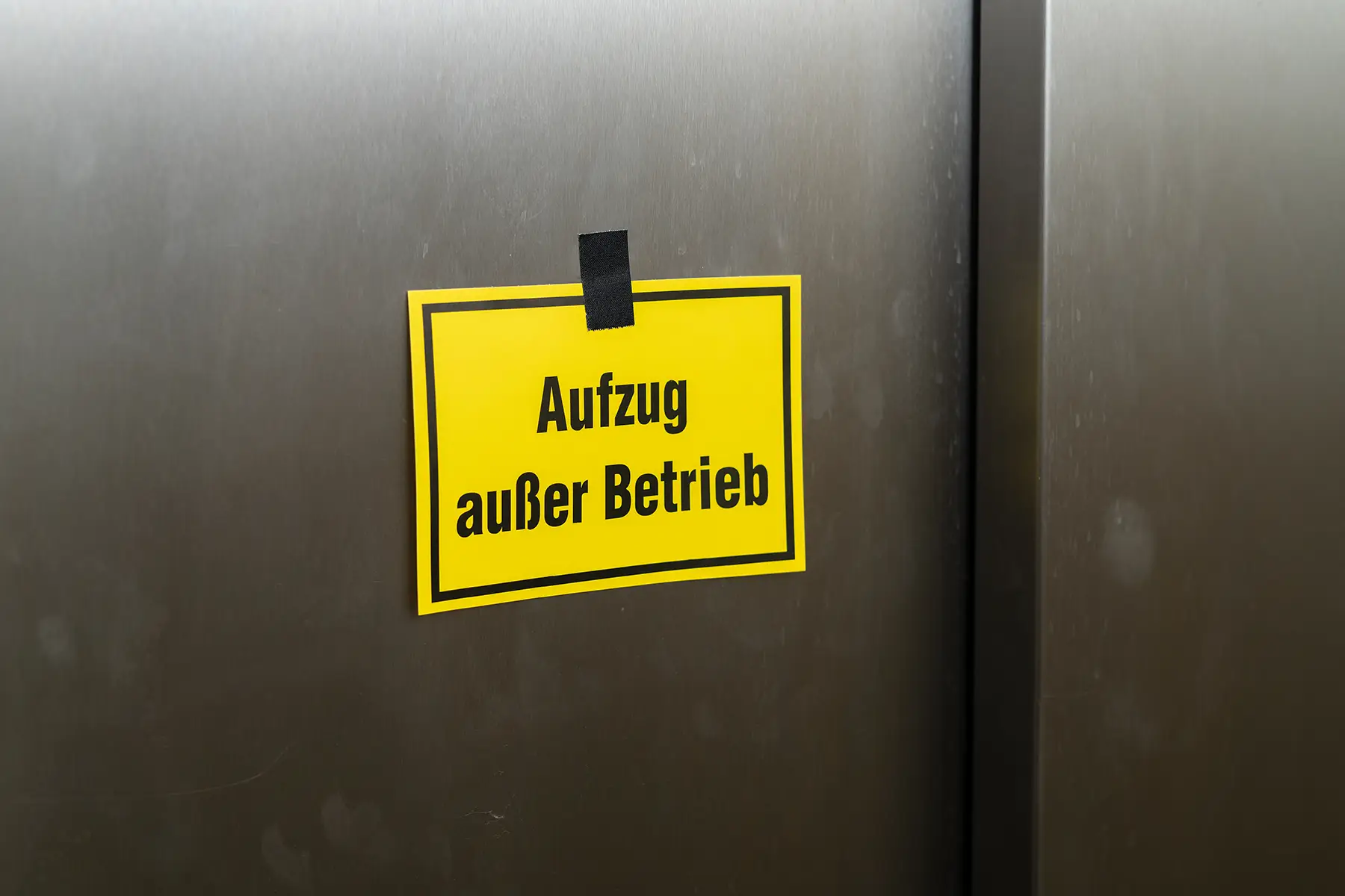 Gelbes Schild mit Aufschrift Aufzug außer Betrieb an geschlossener Aufzugstür